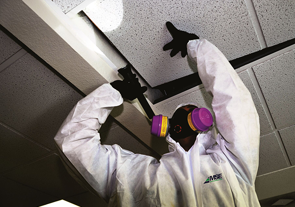 Man in ventilator mask lifting up ceiling tile while conducting Asbestos Testing in New Jersey