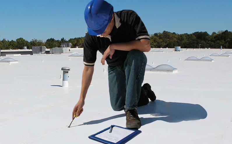Man wearing a blue hard hat inspection the roof of a commercial building in New Jersey