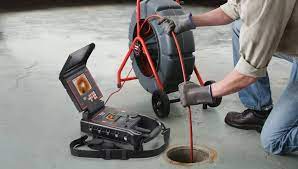 man pushing a video cable down a sewer drain while conduction a sewer inspection